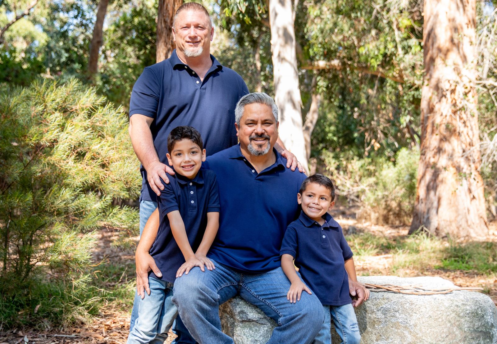 A couple and their sons smiling, surrounded by trees.